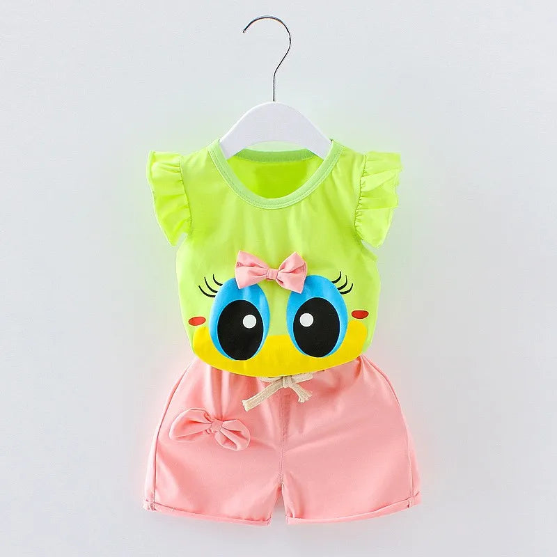 Children's outfit on a hanger: lime green top with large cartoon eyes and pink bow, paired with pink shorts featuring a bow, on a white background.