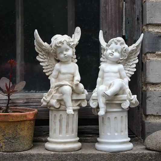 Two marble cherub statues with wings sit on columns by a window. One holds a draped cloth, the other is bare. A potted plant with red leaves is on the left.
