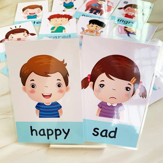 Flashcards depicting emotions, with a boy labeled "happy" and a girl labeled "sad" in front, surrounded by other emotion cards like "scared" and "angry."