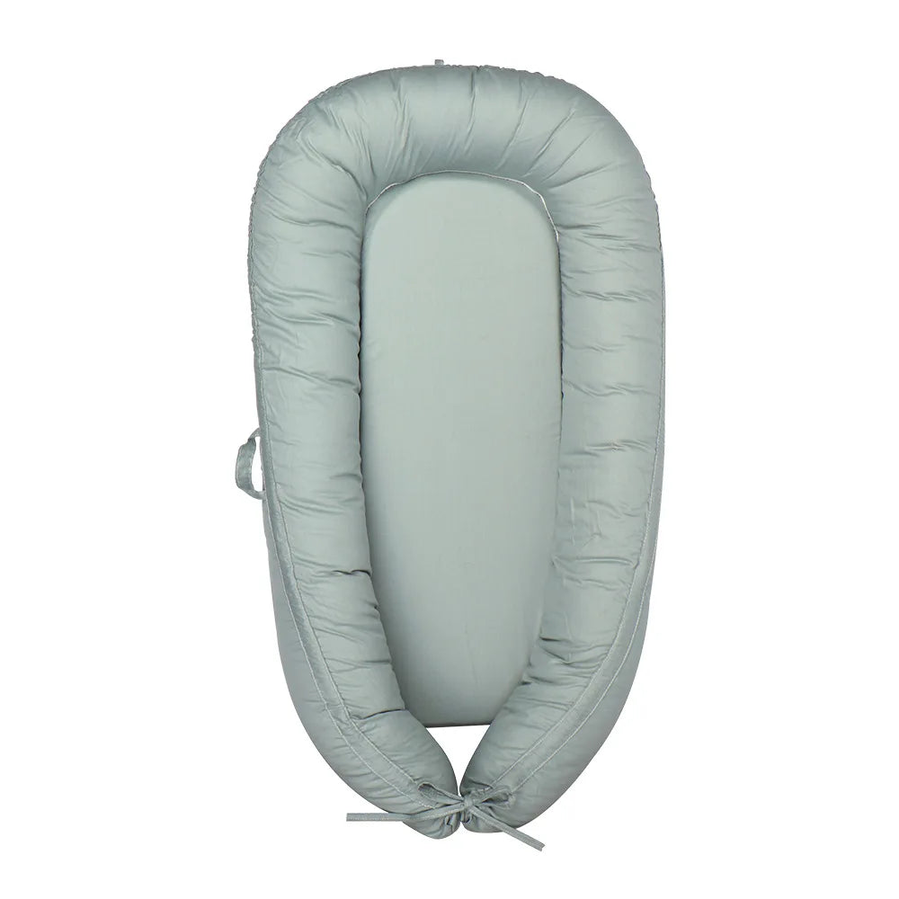 Light gray baby lounger with a soft padded border and an adjustable tie at the bottom. The oval shape provides a snug, secure environment for an infant.