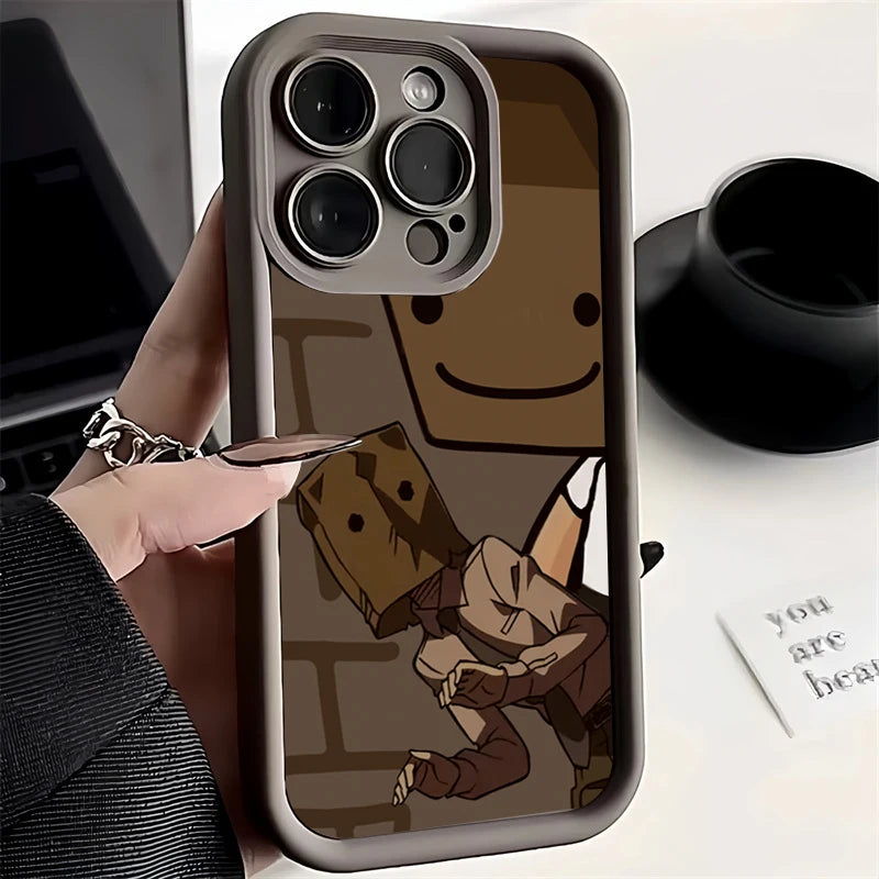 Smartphone in a protective case displaying cartoon characters with paper bag faces. The background includes a laptop and a black cup. A card says "you are beau."