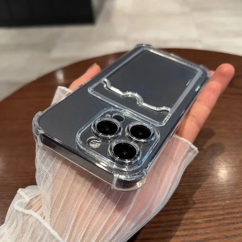 A hand holds a smartphone with a clear case featuring three camera lenses. The phone rests on a wooden surface and the person is wearing a white sheer glove.