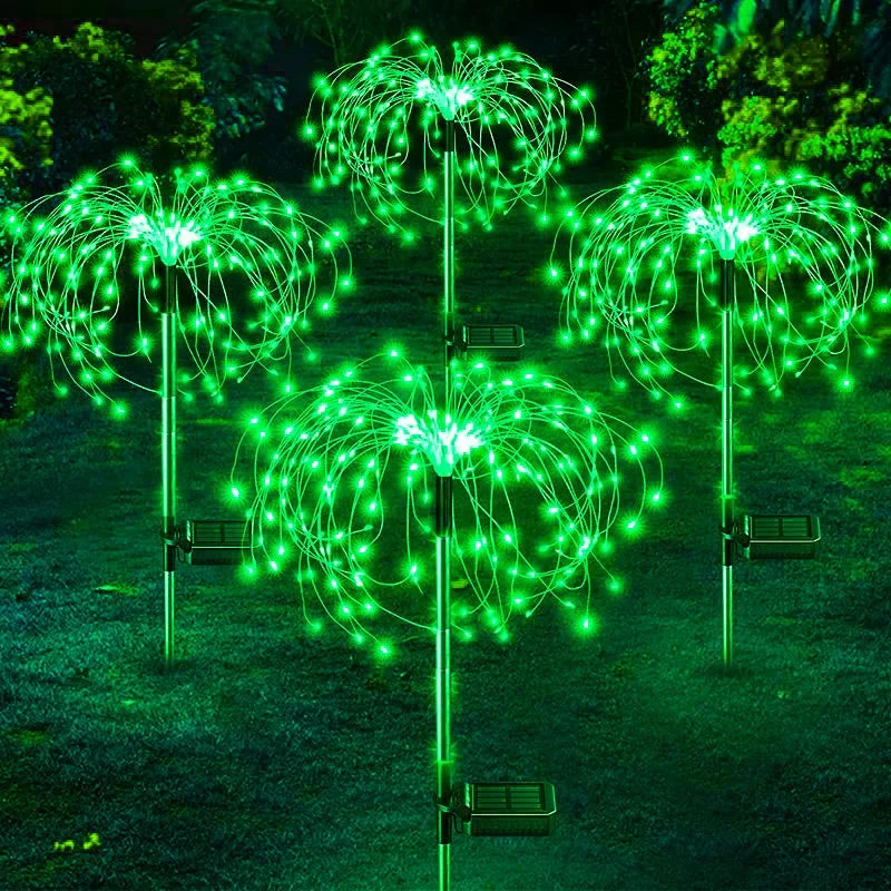 Four solar-powered garden lights shaped like glowing green dandelions illuminate a grassy area against a leafy, dark background, creating a decorative, vibrant display.