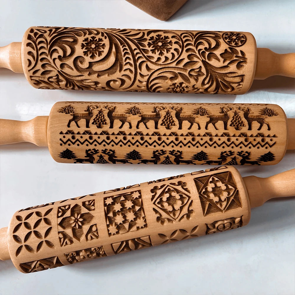 Three intricately engraved wooden rolling pins are displayed, featuring floral swirls, reindeer with trees, and geometric patterns. Each design is unique and detailed.