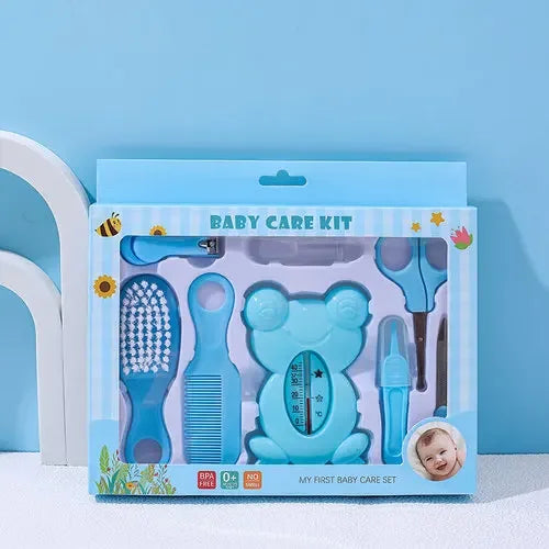 Blue baby care kit with a brush, comb, nail clippers, nasal aspirator, and bear-shaped thermometer in a box labeled "Baby Care Kit." Background includes white arches and a small baby photo.