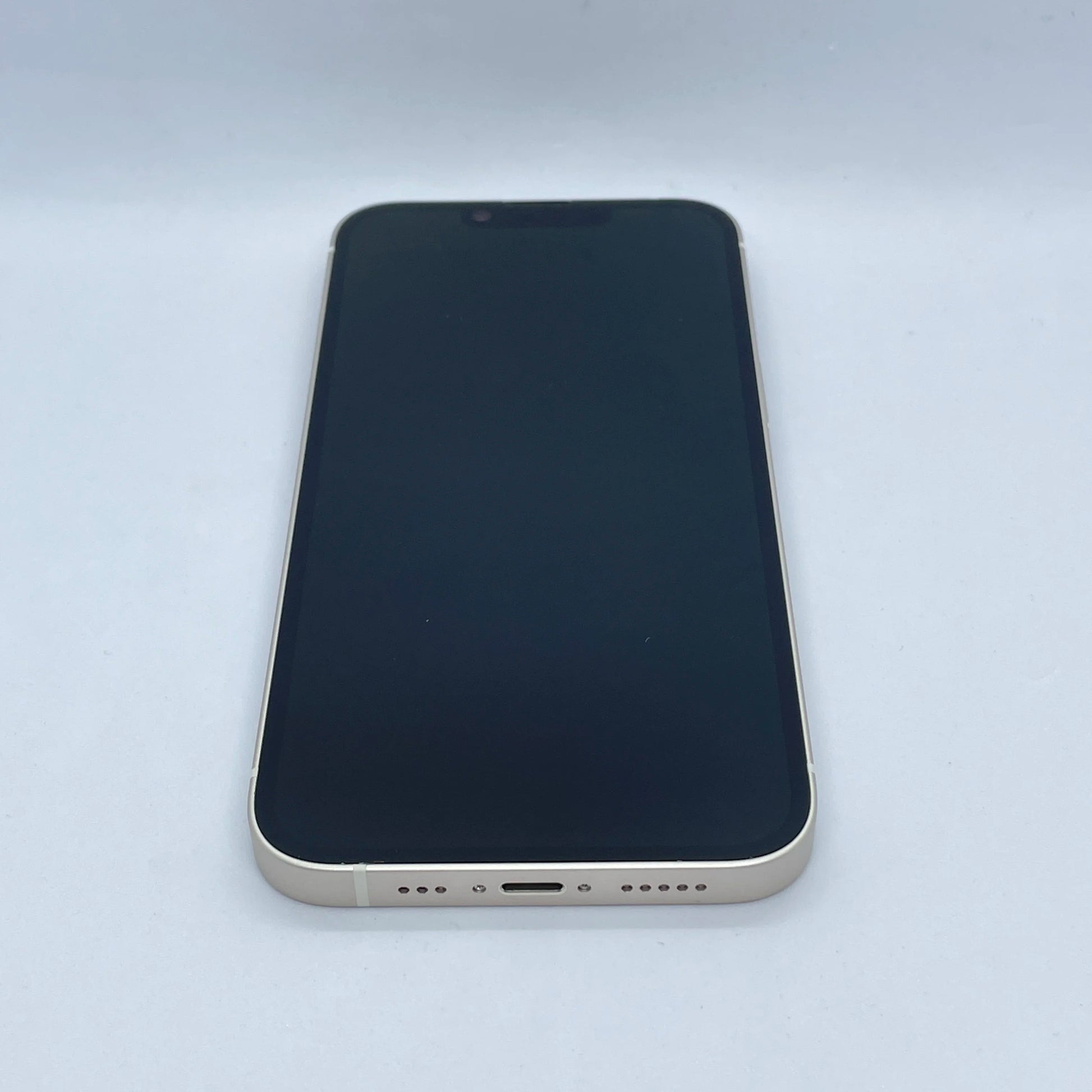 A smartphone with a black screen and gold edges lies on a white surface, showing its bottom edge with a charging port and speaker holes.