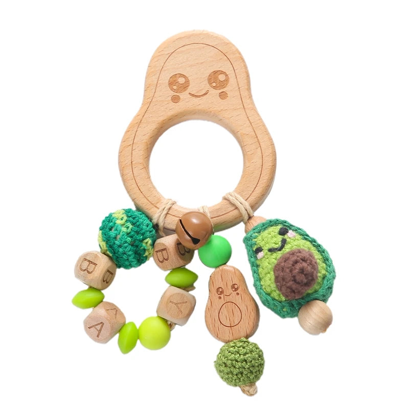Wooden avocado-shaped baby teether with a smiling face, featuring crocheted beads, wooden blocks spelling "BABY," and a green avocado charm.