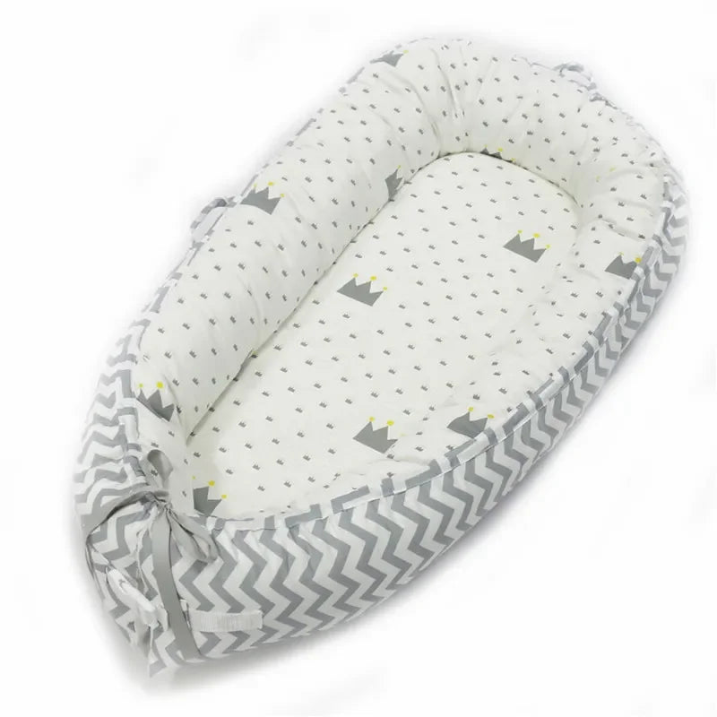 Soft baby nest with gray and white chevron-patterned sides, featuring small gray crowns and dots on the white interior. Comes with adjustable ties at the base.