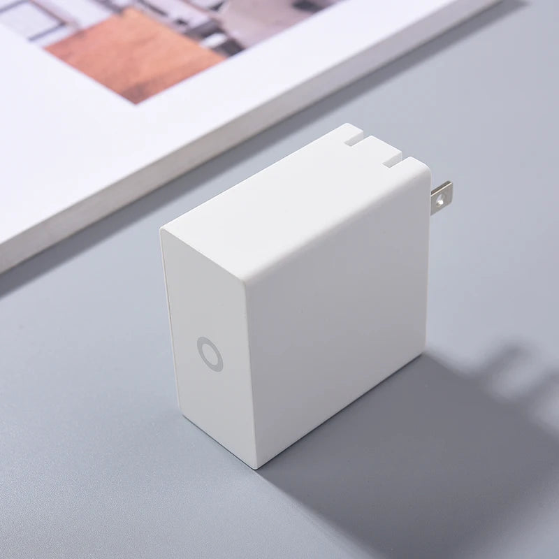 A white rectangular USB wall charger with a circular logo and foldable plug rests on a gray surface near an open photo book.