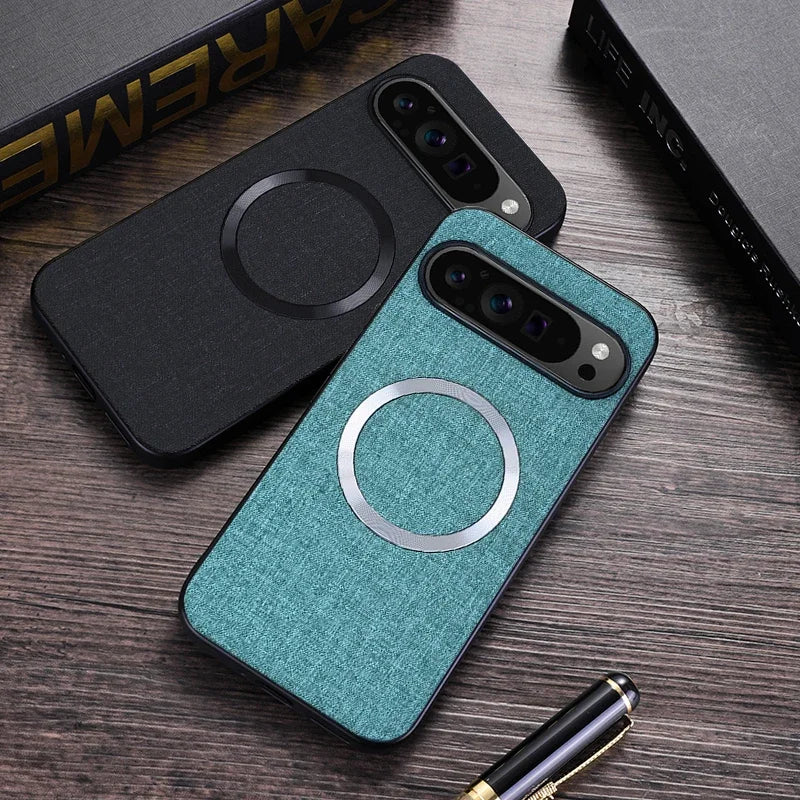 Two smartphones on a wooden table with stylish cases, one black and one blue-green. Both feature a circular design on the back. Nearby is a gold-tipped pen and black book.
