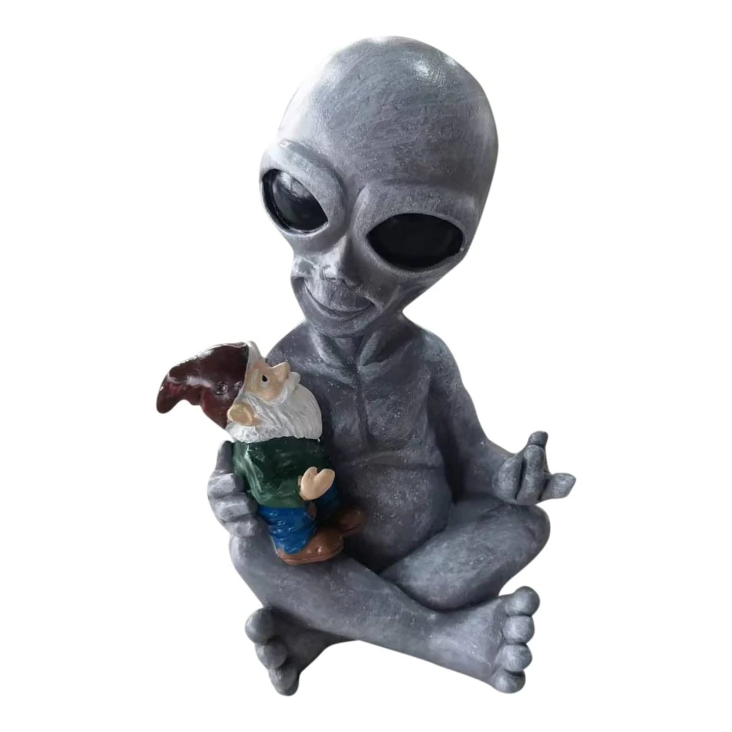 A gray alien figurine in a seated posture holds a garden gnome in its lap. The alien has large black eyes, and its right hand is making a peace sign gesture.