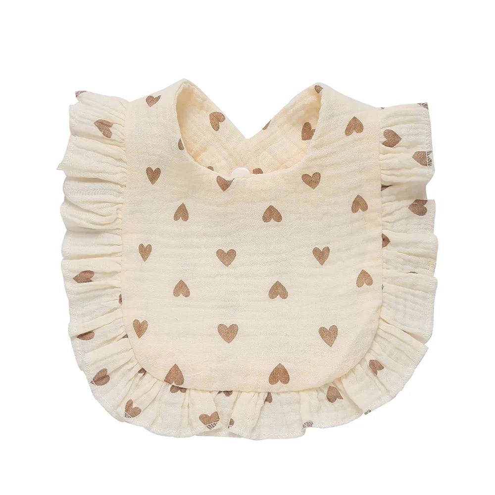 Cream-colored baby bib with brown heart patterns and ruffled edges.