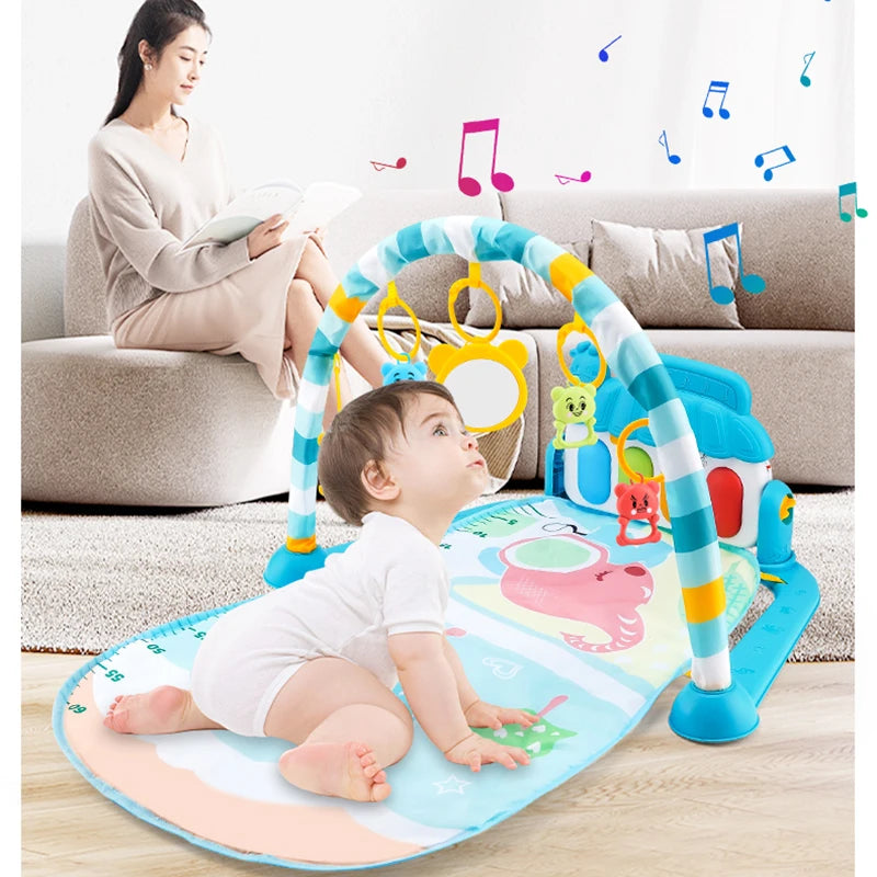 A baby in white clothing is on a colorful play mat with a toy arch, reaching for hanging toys. In the background, a woman sits on a sofa reading a book. Musical notes are illustrated above.