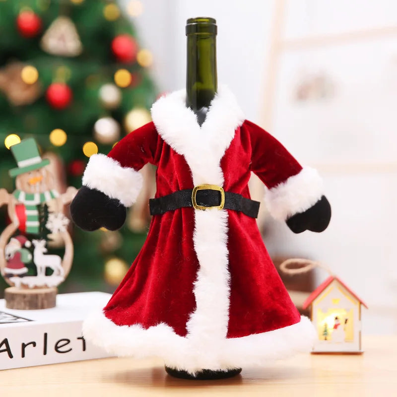 Wine bottle dressed in a Santa Claus outfit with red velvet coat and white trim, set against a blurred background of a Christmas tree with decorative lights and ornaments.