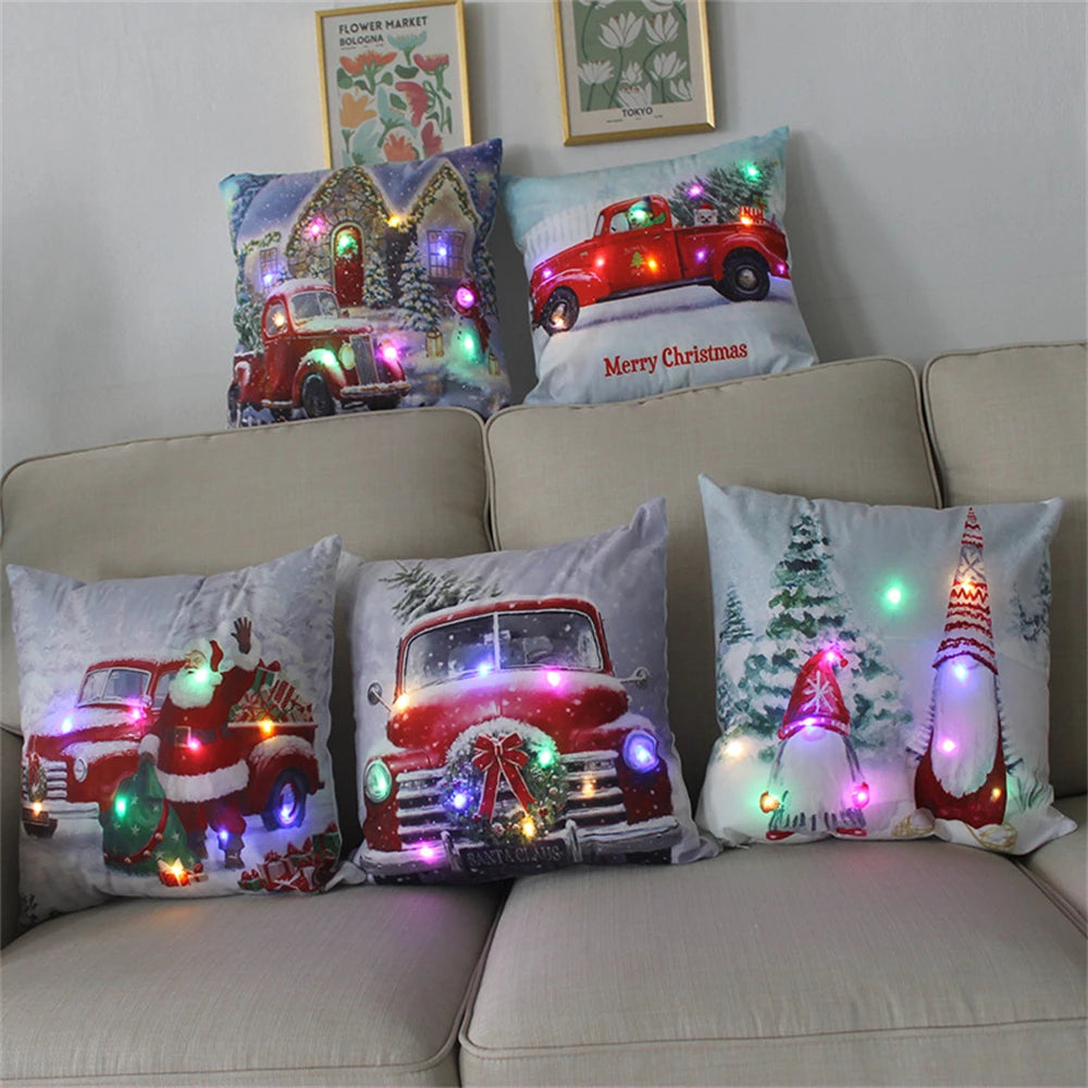 Festive pillows with Christmas-themed designs featuring vintage red trucks and gnomes. Each pillow is adorned with colorful LED lights, set on a beige sofa.