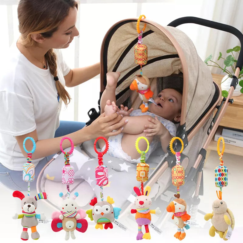 A woman attends to a baby in a stroller adorned with colorful hanging plush toys, including an owl, butterfly, and other animals. The setting is bright and homey.