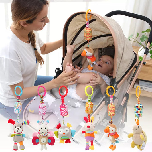 A woman attends to a baby in a stroller adorned with colorful hanging plush toys, including an owl, butterfly, and other animals. The setting is bright and homey.