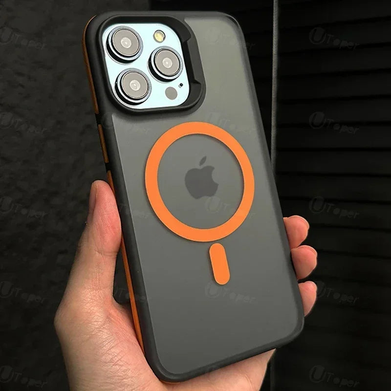 A person holds a smartphone with a gray case featuring an orange MagSafe ring. The phone has three camera lenses and an Apple logo. The background is a dark, textured surface.