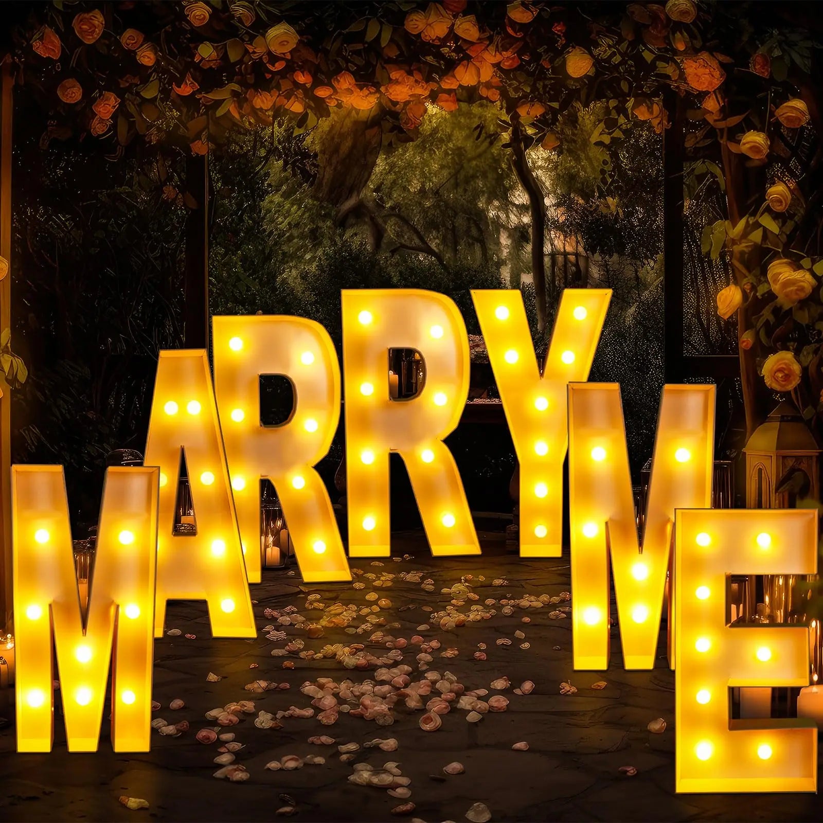 Illuminated letters spell out "MARRY ME" in a romantic setting with rose petals on the ground and flowers above, creating a warm and inviting atmosphere for a proposal.
