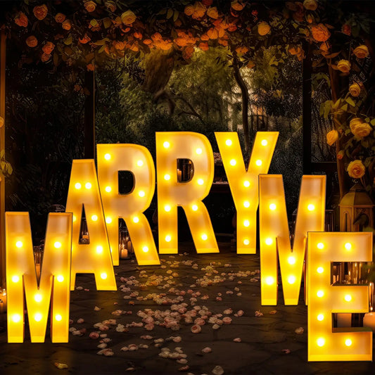 Illuminated letters spell out "MARRY ME" in a romantic setting with rose petals on the ground and flowers above, creating a warm and inviting atmosphere for a proposal.