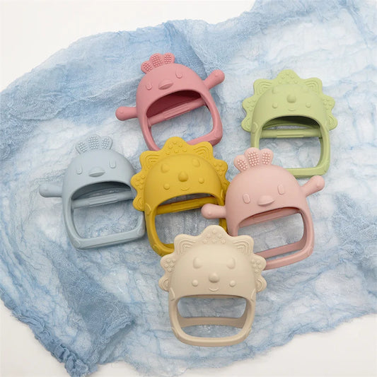 Colorful silicone baby teethers shaped like cartoon characters are arranged on a soft blue cloth. The teethers are in pastel shades of blue, pink, green, yellow, and beige.