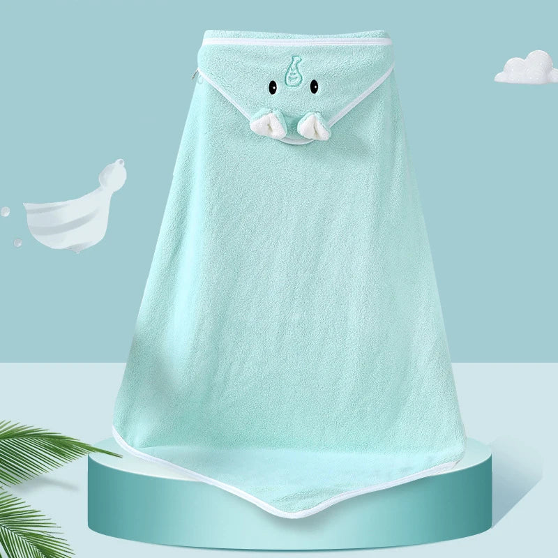 A light blue hooded baby towel with an adorable face design and ears, displayed on a cylindrical platform. The background features clouds and a leaf in soothing pastel tones.