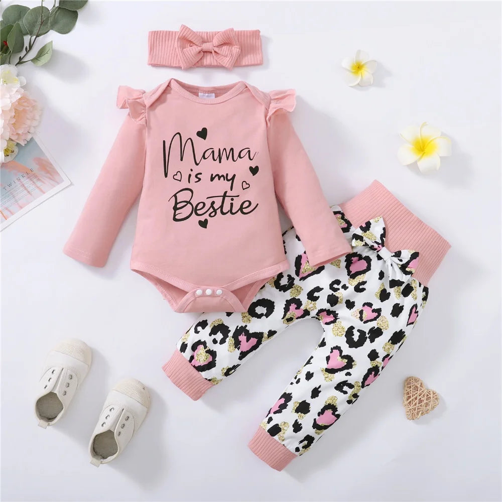Pink baby outfit with "Mama is my Bestie" on the bodysuit, paired with leopard print pants. Includes a matching pink bow headband and white shoes, surrounded by flowers and a heart.