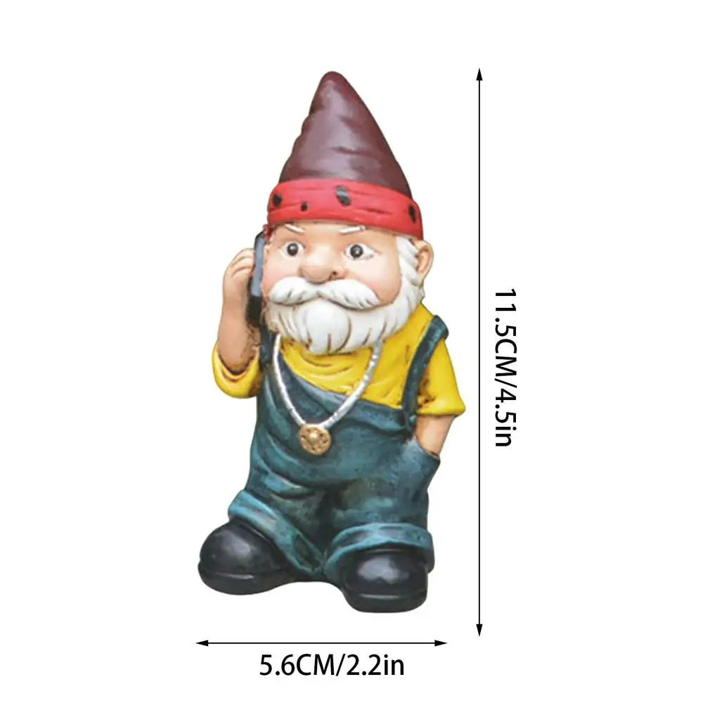 A garden gnome wearing a red hat and yellow shirt with denim overalls, holding a phone. Dimensions displayed: 11.5 cm tall and 5.6 cm wide.