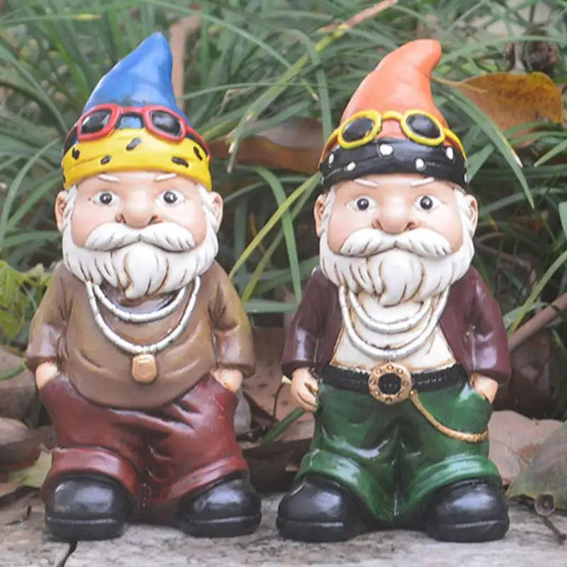Two garden gnomes with beards and colorful hats, wearing necklaces and sunglasses, stand on a stone surface with greenery in the background.