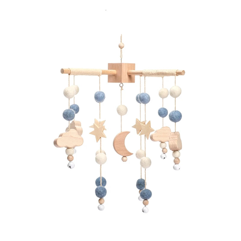 Wooden baby mobile featuring felt balls in blue and white, with suspended stars, moon, and cloud shapes. Hanging from a wooden crossbar with a minimalist design.