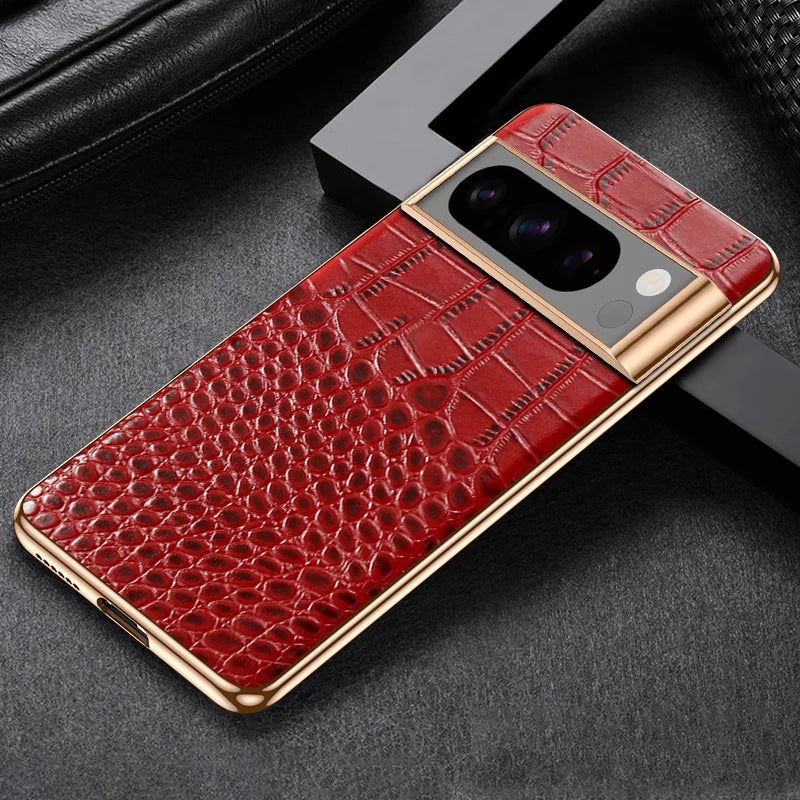 A smartphone with a luxurious red crocodile pattern case and gold accents is placed on a dark textured surface near a black leather item. The camera module is prominent.