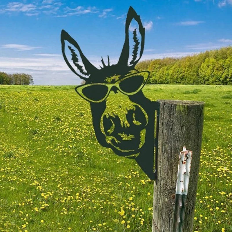 Silhouette of a donkey with sunglasses on a wooden post in a sunny field with yellow flowers and a blue sky.
