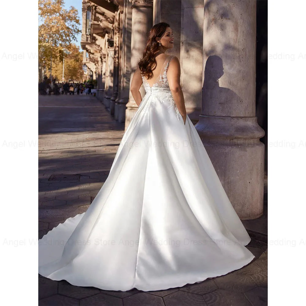 Bride in an elegant white gown with lace details on the back, standing on a sunlit stone path surrounded by columns. The scene captures a serene, joyful moment.