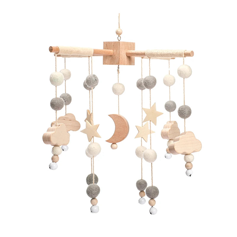 Wooden baby mobile with stars, clouds, and crescent moon, adorned with gray and white felt balls and tiny bells, hanging from a wooden dowel with wrapped ends.