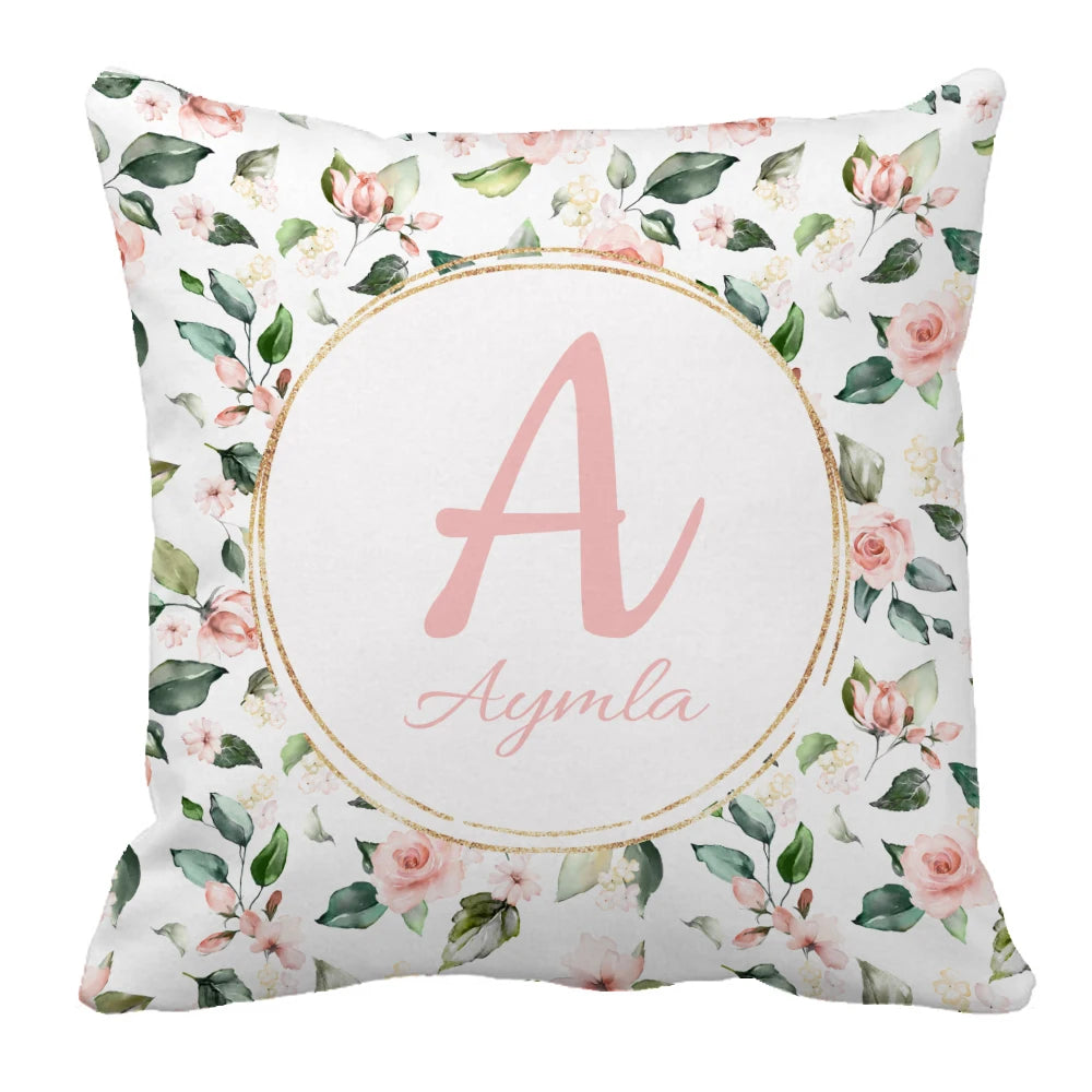 Floral cushion with pink roses and green leaves, featuring a central gold-rimmed circle with a large pink letter "A" above the name "Aymla."