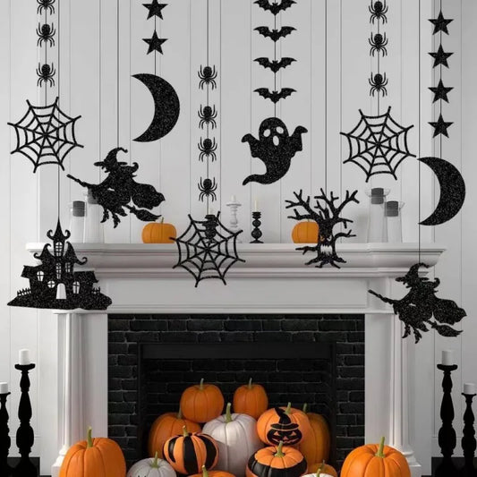 A white mantle decorated for Halloween with hanging silhouettes of witches, ghosts, bats, spiders, stars, cobwebs, and moons. Orange pumpkins, some with black designs, are placed on and around the mantle. Black candle holders add to the festive and spooky ambiance.