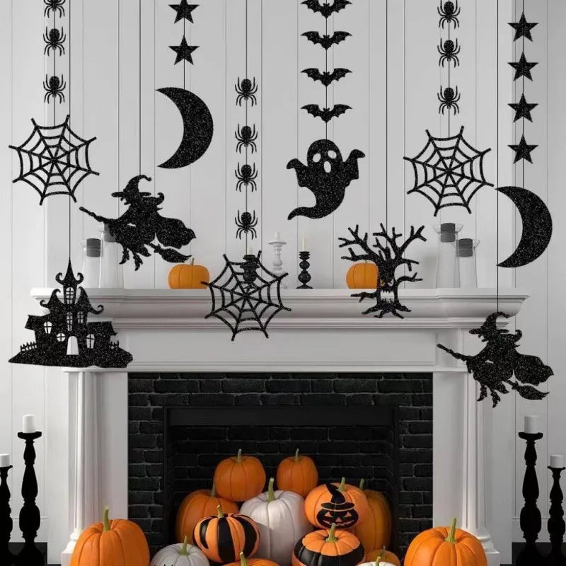 Halloween-themed mantel with hanging decorations, including witches, bats, spiders, ghosts, crescent moons, webs, and stars. Pumpkins and candlesticks adorn the mantel and hearth, enhancing the spooky atmosphere. The color scheme features black and orange against a white backdrop.