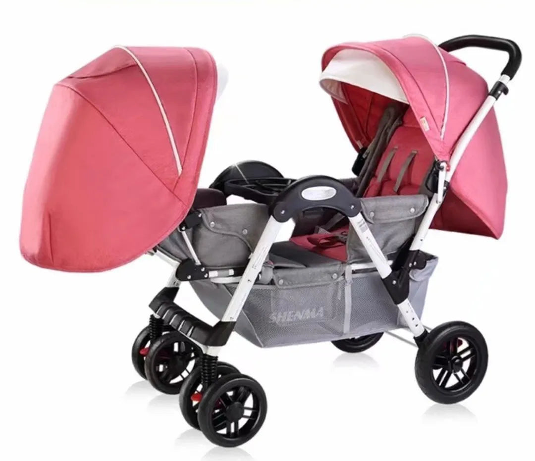 Pink double stroller with adjustable canopies, sturdy black wheels, and a grey frame. The seat design includes multiple recline positions for comfort.