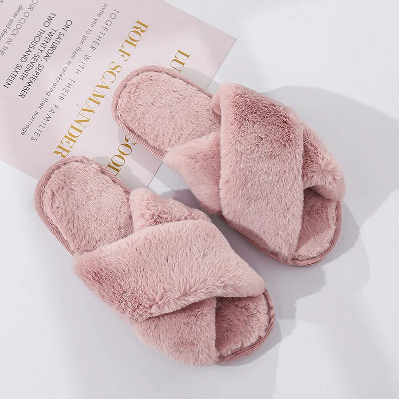 Pink fluffy cross-band slippers on a white surface, partially covering a printed invitation with gold and black text.