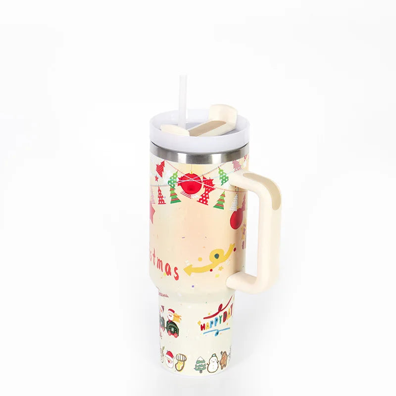 Festive travel mug with Christmas-themed design, featuring ornaments, trees, and cartoon characters. It has a handle, a lid with a straw, and a colorful, cheerful pattern.