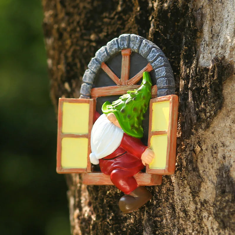 A gnome figurine with a green pinecone hat and red outfit sits in a miniature window frame attached to a tree trunk. The window has open shutters and a stone arch.