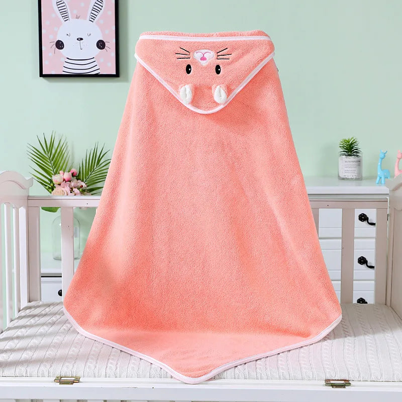 A peach hooded baby towel with a cute animal face and ears hangs on a crib. The room features a pastel green wall, bunny artwork, and a dresser with plants.