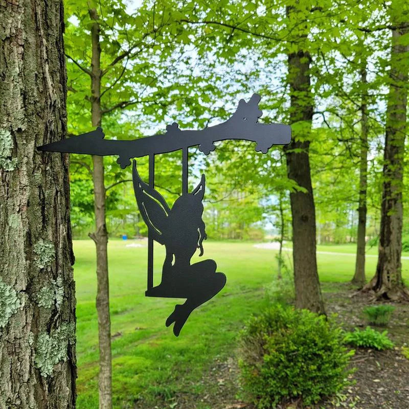 Silhouette of a fairy swinging from a branch attached to a tree trunk in a lush green forest, with a blurred background of grass and more trees.