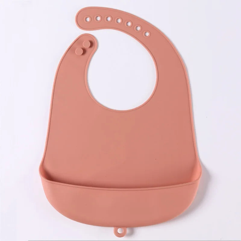 Peach-colored silicone bib with adjustable neck strap and a deep spill pocket, designed for babies to catch food and drink spills during meals.