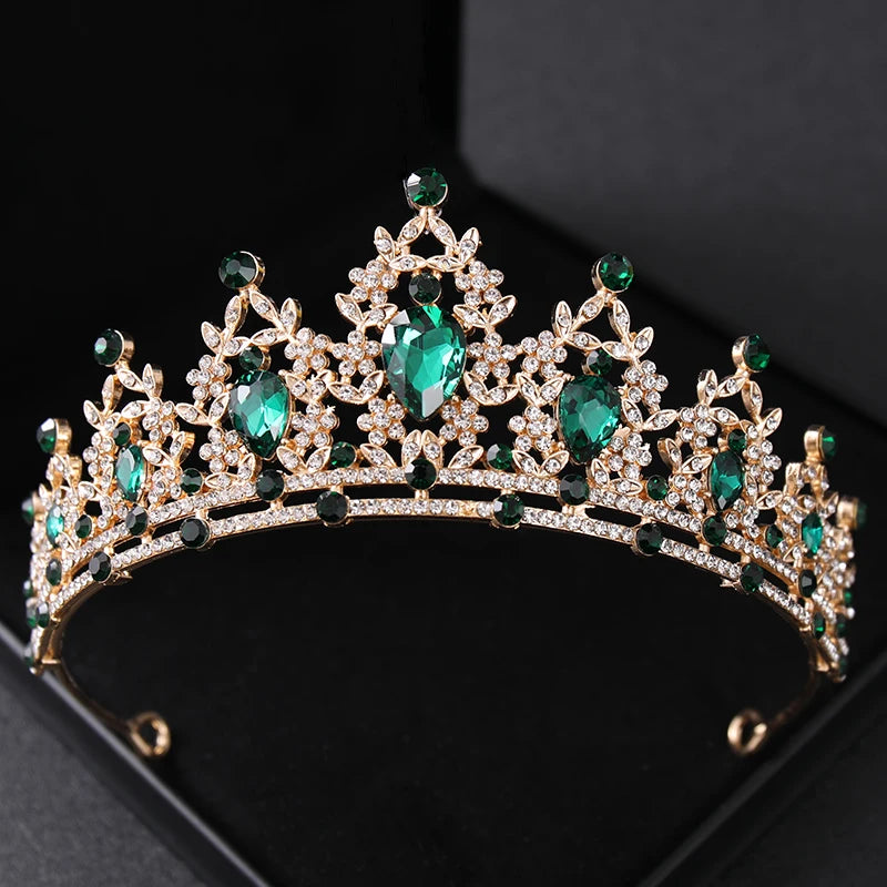 Gold tiara adorned with intricate patterns of sparkling diamonds and large emerald gemstones, displayed on a black background.