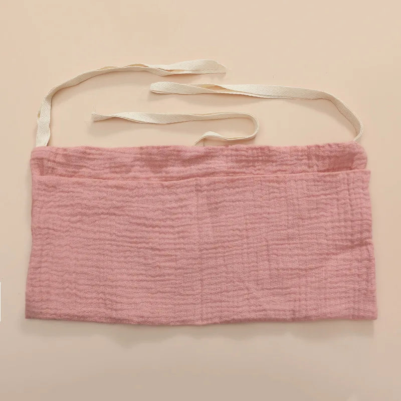A pink textured fabric belt with off-white ties, laid flat on a beige background. The belt features a soft, crinkled texture and is designed for wrapping or tying.