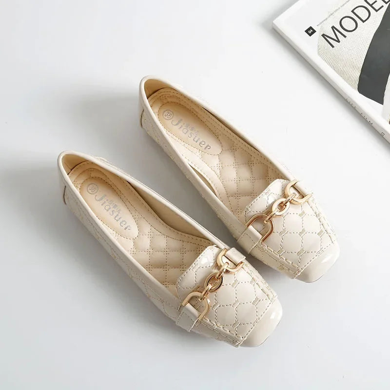 Cream-colored quilted loafers with gold chain detailing, placed on a white surface beside a black-and-white magazine.