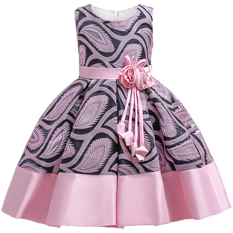 Pink and purple sleeveless dress with a leaf pattern, featuring a satin sash with rose and ribbon accents at the waist. The skirt has a wide solid pink hemline.