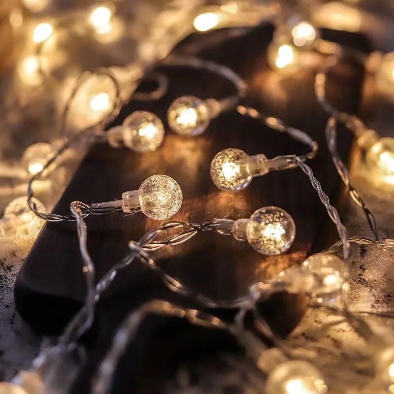 Warm white fairy lights with round bulbs are tangled on a dark wooden surface, casting a cozy, ambient glow.