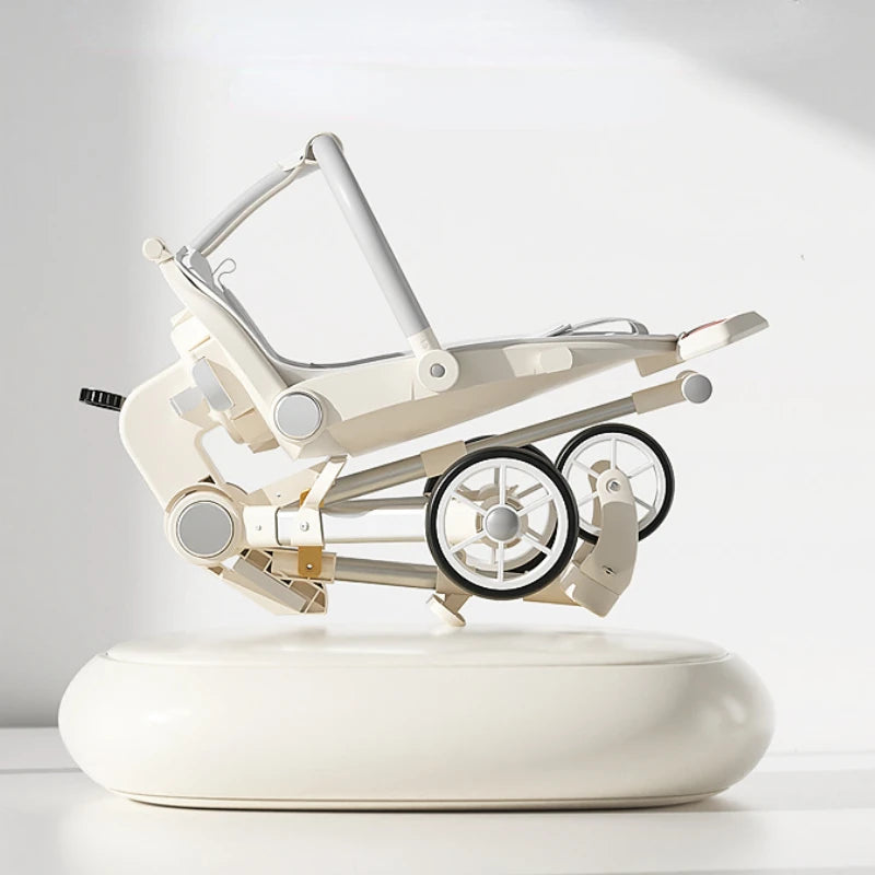 A compact, foldable stroller with a modern design is displayed on a white surface. It features a sleek beige frame, gray handles, and dual wheels, highlighting its portability.